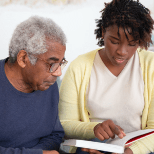 A black woman reading a book to an old man